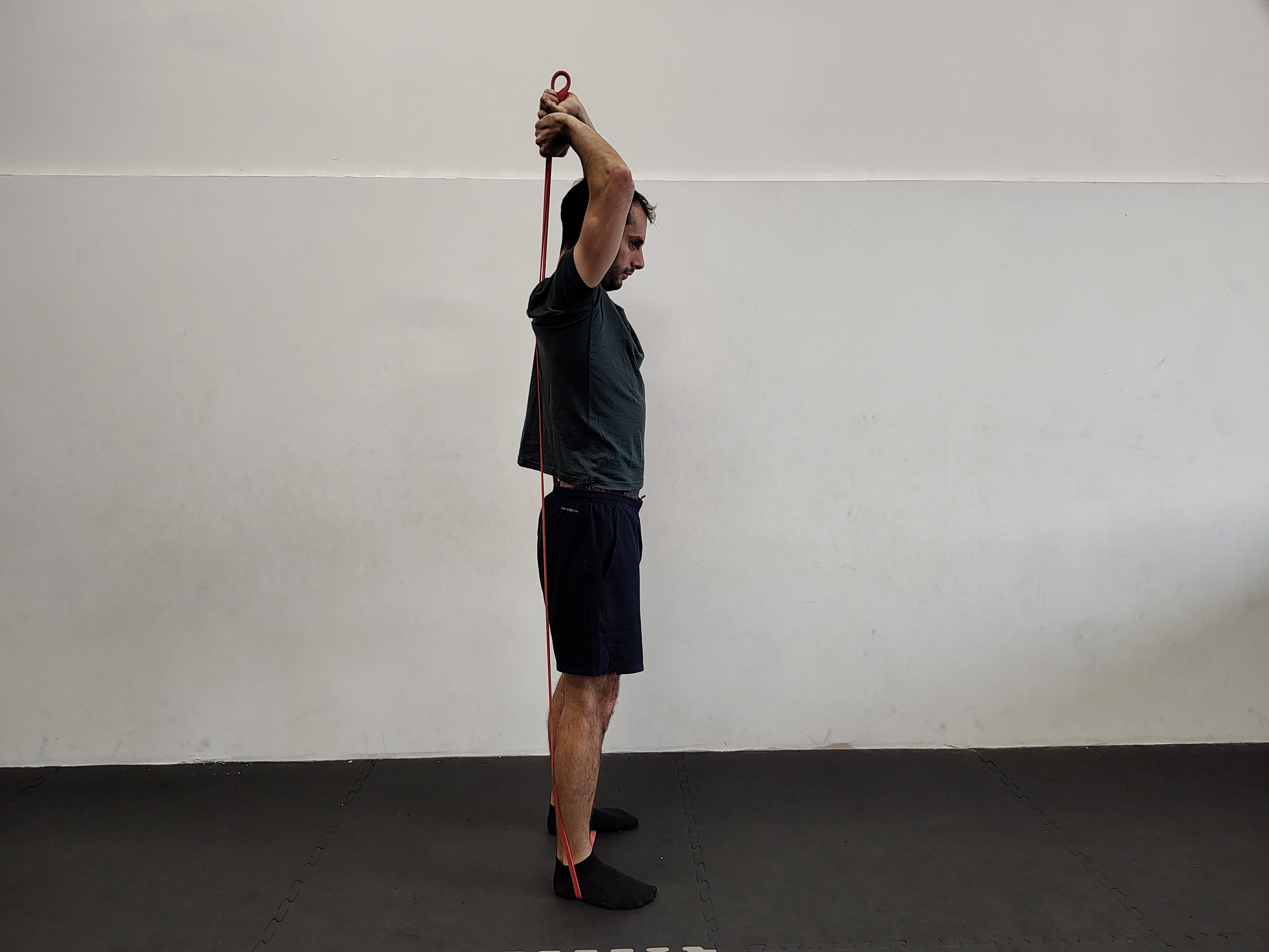 Muž v tělocvičně cvičí tricepsové zdvihy s expandérem.